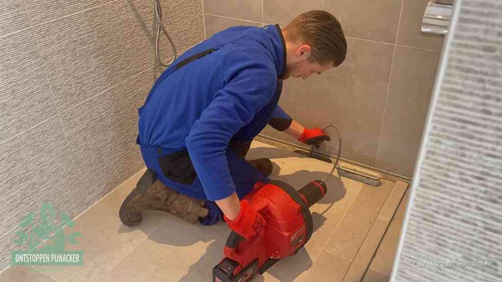 Een monteur ontstopt een langwerpige douchegoot met een elektrische veer, een doucheputje verstopt door haren en zeep in Pijnacker