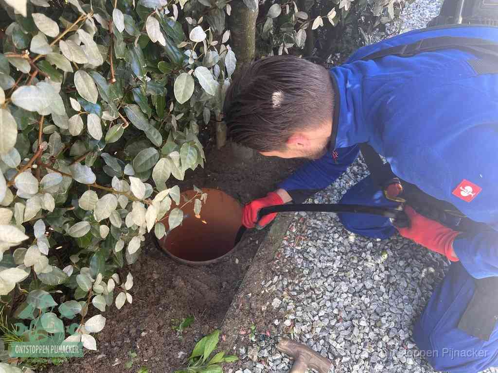 Een monteur voert een slang in een geopende rioolput in de tuin om het hoofdriool te ontstoppen in Pijnacker