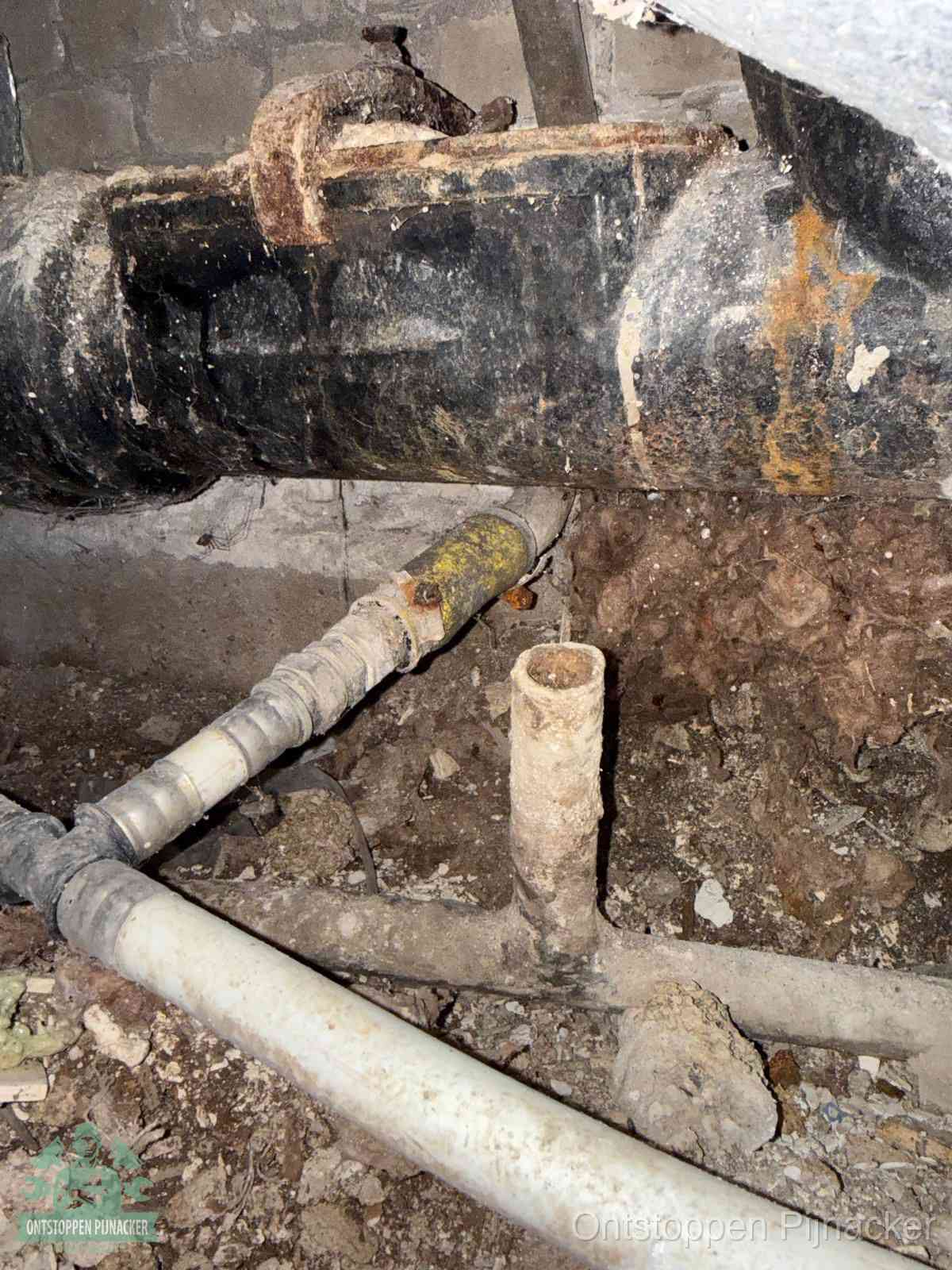 Een oude hoofdrioolbuis met roest- en kalkaanslag in een kruipruimte, oorzaak van terugkerende structurele rioolproblemen in Pijnacker